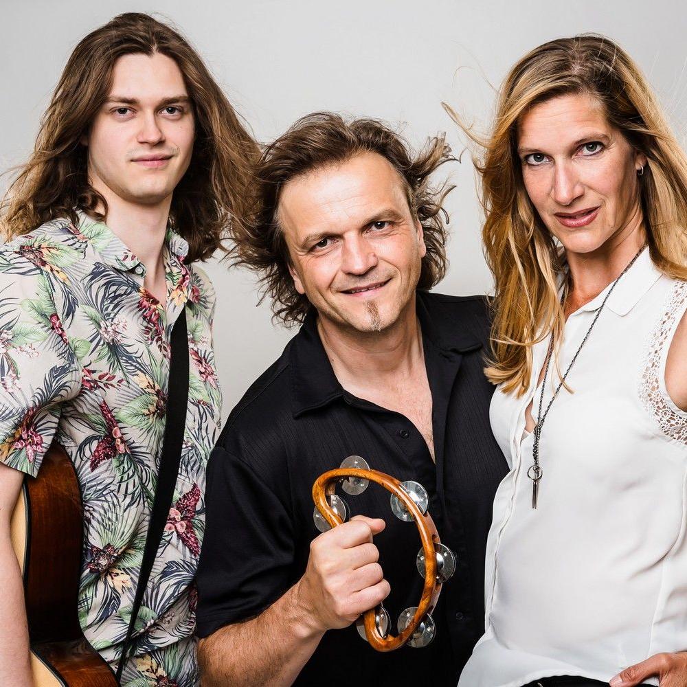 Promofoto auf dem Anton mit seiner Gitarre, Dirk mit einem Schellenkranz und Stephanie im weißen Shirt zu sehen sind